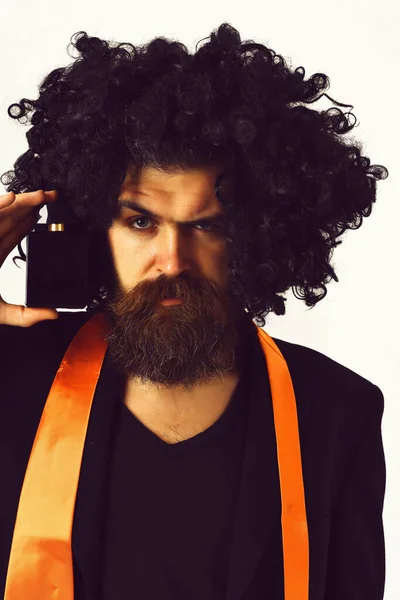 Caucasian hipster in suit and black curly wig holding perfume — Stock Photo, Image