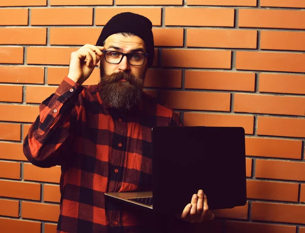 Brodaty brutalny biały hipster trzyma laptopa na brązowej cegły ściany studio tła — Zdjęcie stockowe