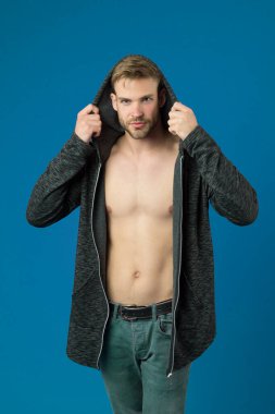 Gülen suratlı adam kapüşonlu, mor arka planlı ceketi deniyor. Yüzünde kıllar, göğsünde pürüzsüz bir deri olan adam giyinmeye çalışıyor. Moda konsepti. Adam uzun kapüşonlu ceketle çekici görünüyor.