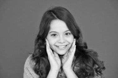 Mutlu bir çocukluk. Güzel model çocuk. Moda konsepti. Saçlar için en iyi şampuanlar ve saç kremleri. Donuk ve hasarlı saçlar. Uzun kıvırcık saçlı kız. Küçük güzel, gülümseyen kırmızı arka plan