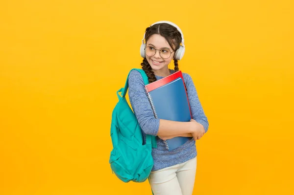 Menina estudante moderna com mochila e escola fornece fundo amarelo, conceito de lições de áudio — Fotografia de Stock