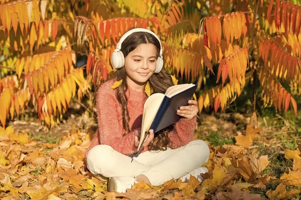 Girl read book on autumn day. Autumn literature concept. Child enjoy reading. Studying twice faster using visual and audio information. Little child enjoy learning in autumn park. Kid study with book