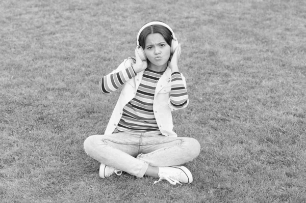 Bambino felice ascoltare musica in cuffia. piccola ragazza su erba verde. il bambino gode la canzone nella natura del parco. concetto di infanzia felice. utilizzare il dispositivo digitale nella vita moderna. studentessa relax all'aperto — Foto Stock