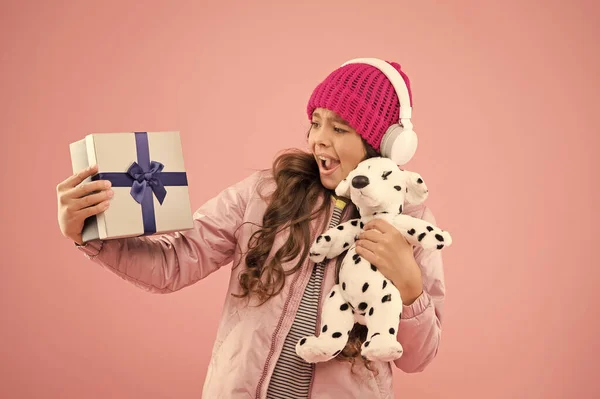 Joyeux concept d'enfance. Meilleurs cadeaux pour les adolescentes. Élégant écolière jouer avec jouet pour chien et tenir boîte cadeau. Fille petite mignonne à la mode avec écouteurs portent jouet doux. Prenez le jouet préféré avec vous — Photo