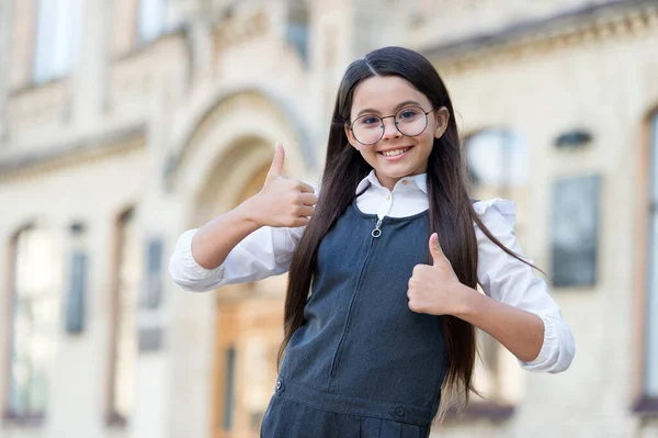 Bambino felice in uniforme scolastica dare pollici in alto gesto della mano nel cortile della scuola all'aperto, approvazione. buona istruzione — Foto Stock