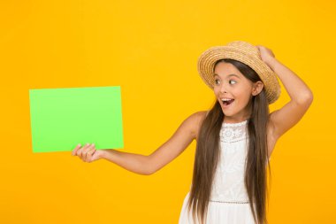 Yeni haberleri paylaşıyoruz. Çocuklar için plaj modası. Sarı arka planda küçük bir çocuk. Yaz kampı aktivitesi. kopyalama alanı. Yaz tatili ve tatil. Mutlu çocukluk. Şaşırmış küçük kız kağıt çarşaf tutuyor.