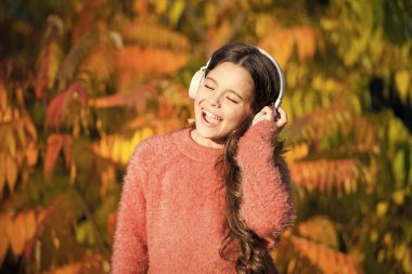 Güzel şarkılarla sonbahar yürüyüşleri. Sonbahar havası için müzik. Dinleme şarkısı. Sonbahar gününün tadını çıkar. Sesi dinlemenin en iyi yolu çocuğun kelime dağarcığını geliştirmesine yardımcı olmaktır. Kulaklıklarıyla sonbahar ağacının yanında dinlenen kız çocuğu.