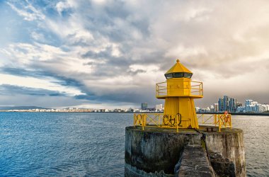 Reykjavik İzlanda 'daki rıhtımdaki deniz feneri. Deniz feneri sarı parlak kule deniz kıyısında. Deniz limanı navigasyon konsepti. Deniz ulaşımı ve seyrüsefer. Deniz manzarası ve parlak deniz feneriyle gökyüzü