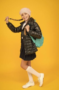 Çok sevimli bir öğrenci. Sonbahar kışı. Okul sezonu için kıyafet al. Liseli kız moda kıyafeti. Sırt çantalı çocuk. Moda dükkanı. Moda konsepti. Kız örgü şapka ve ceket giyiyor. Sarı arka plan.