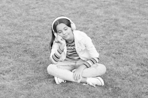 Podcast educativo. Haz que suceda. Escucha música mientras te relajas al aire libre. Niña disfrutar de la música pradera hierba verde. Es un buen momento. Los auriculares infantiles escuchan música. Cool chica auriculares escuchar música — Foto de Stock