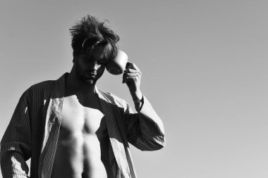 Mavi çizgili pijamalı, elinde fincanla beyaz maço.