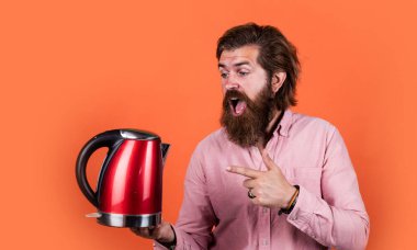 Şuna bak. Oda servisinde kullanışlı. Olgun karizmatik erkek elektrikli su ısıtıcısı kullanır. Sakallı ve bıyıklı adam çay yapıyor. Sıcak çay iç. Sakallı adam mağaza asistanı mutfak aletlerini sunar.