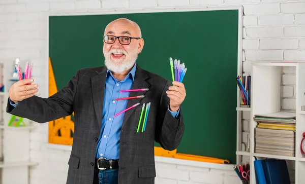 每天写信。高级教师手里拿着五彩缤纷的钢笔。选择任何颜色。快乐的胡子老师。回学校去有板的教室。学校写作物品购物。男人使用许多办公工具 — 图库照片
