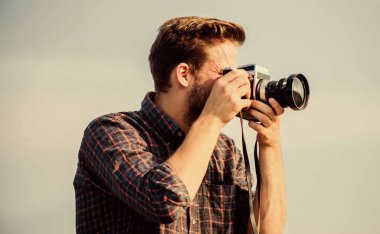 Adam açık havada gökyüzü arka planında. Yakışıklı blogcu, gezgin, geçmişe dönük kamera. Gazeteci fotoğraf çekiyor. Elle ayarlar. Gezgin blogcu. Antika ekipmanlar. Hippi fotoğrafçı. Blogger vurucu vlog
