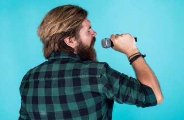 Melodiyi yakala. Olgun karizmatik erkek vokalist. Mikrofonda şarkı söyleyen sakallı adam. Sahnede özgüven ve karizma. Kareli gömlek giyen sakallı bir adam. Rock müzik. Erkek karaoke şarkıcısı