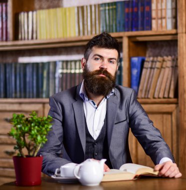 Sakallı bir adam elinde çay fincanıyla kitap okuyor.