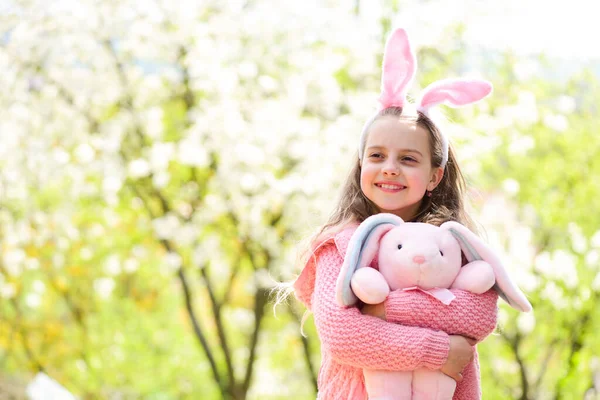 Helgfirande koncept Påsk och vår. Lycklig flicka som håller rosa kanin i trädgården med blommande träd. — Stockfoto