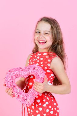 Göz kırpan kız pembe arka planda pembe kalbi tutuyor.