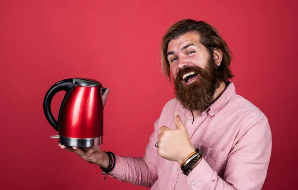 Un sourire de célibataire. homme va boire du thé ou du café. homme brutal avec moustache et barbe. appareil électroménager. homme barbu utiliser bouilloire électrique rouge. concept de ménage masculin. besoin d'eau chaude — Photo