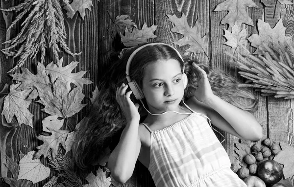 Enjoy music and relax. Enjoy perfect sound. Girl lay fallen leaves wooden background. Music application for youth modern gadget. Child girl listen music headphones top view. Autumn music playlist