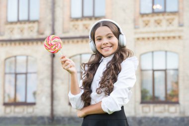 Kulaklık takan retro çocuk lolipopu tutuyor. Öğrenci müzik dinler. Okula dönüyorum. Şekerli güzellik. Çocuk eğitimde yenilik yapıyor. Mutlu çocuklar günü. Tatlı onu mutlu ediyor. okul kızının modern görünüşü