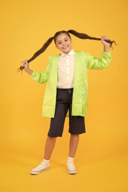 Su geçirmez konsept. Sevimli çocuk. Mutlu liseli kız sarı arka planda yağmurluk giyiyor. Küçük liseli kızlar yağmurlu günlerde suya dayanıklı kıyafetler giyerler. Tatlı liseli kız kendini bahar havası için korunmuş hissediyor.