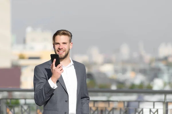 Feliz hombre de negocios con smartphone en terraza soleada. Hombre sonrisa en traje formal con teléfono móvil al aire libre. Comunicación empresarial y nuevas tecnologías. Concepto de estilo de vida — Foto de Stock