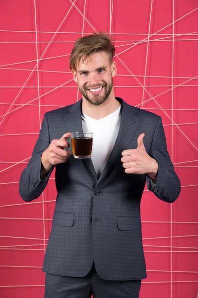 Man formal elegant suit shows thumb up gesture. Bachelor elegant guy drink tea or coffee and highly recommend good quality product. Morning coffee concept. Satisfied with hot beverage in glass cup