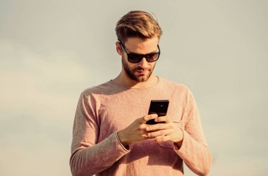 Hippi güneş gözlüğü takıyor cep telefonuyla gökyüzü arka planı tutuyor. Hippi akıllı telefon görüşmesi. Adam cep telefonu. İrtibatı koparmayalım. Mobil çağrı konsepti. Önemli bir cep telefonu sohbeti. Uygulama ve internet