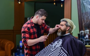 Kendini talep et. Kuaförde olgun bir adam. Saç bakımı ve erkek bakım konsepti. Formunu koru. Sakallı adam berbere sakal tıraşı oluyor. Bıyık ve sakal. Kuaförde sandalyede oturuyor.