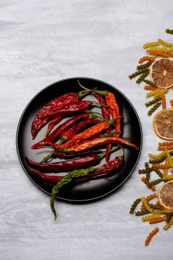 Kırmızı biber ve siyah seramik tabak içinde makarna ve malzemeler.