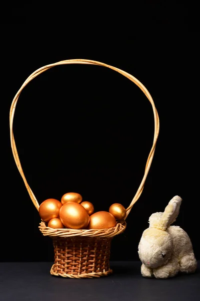 Eggs painted in golden color inside basket with rabbit toy — Stock Photo, Image