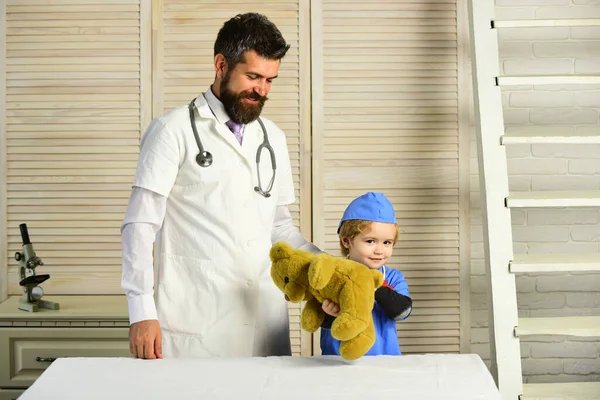 Hombre con barba y niño con batas médicas sostienen oso — Foto de Stock