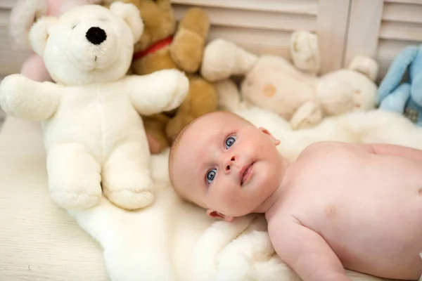 Niño y oso de peluche. Bebé acostado en edredón blanco — Foto de Stock
