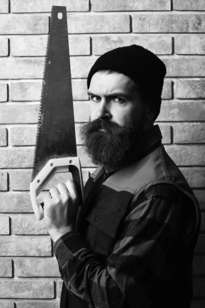 Бородатый строитель держит пилу с серьезным лицом — стоковое фото