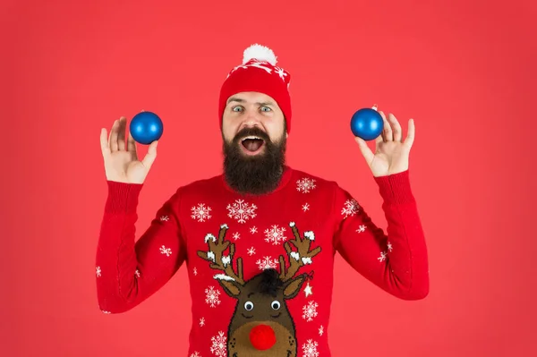 New year concept. Christmas party. Winter outfit. Good vibes. Festive decorations. Essential winter activities for families. Hipster bearded man wear winter sweater and hat hold balls red background — Stock Photo, Image