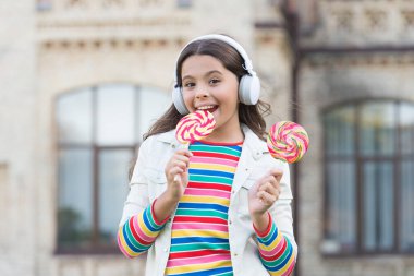 Neşeli kız modern kablosuz kulaklıklar şeker yer, lezzetli lolipop konsepti