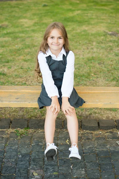 För din lilla förtjänar det. Glada barn sitter på bänken utomhus. Skolutseendet på barnflickan. Formellt mode. Enhetlig klänning. Grundskola. Barnomsorg och barndom. Internationella barnens dag — Stockfoto