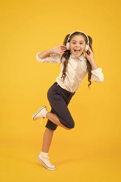 Idealna piosenka dla aktywnych dzieci. Szczęśliwa dziewczynka porusza się aktywnie do muzyki. Aktywny uczeń biegnący do szkoły na żółtym tle. Aktywny i energiczny mały dzieciak słuchający muzyki w słuchawkach — Zdjęcie stockowe