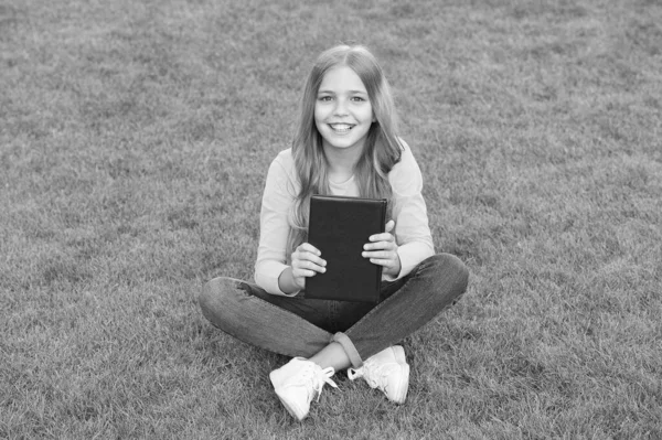 Teenie-Mädchen begeistert mit neuem Buch. Entspannen auf grünem Gras. Frühlingsfreizeit. glückliche Kindheit. Kind liest Buch im Freien im Park. glückliche kleine Mädchen studieren im Urlaub. Schönheit und Mode für Kinder — Stockfoto