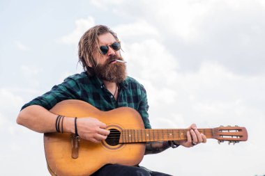 Sigara içiyorum. Sıradan bir erkek gitarist. Müzik ve vokal konsepti. Akustik gitar çalan bir adam. Bıyıklı ve sakallı vahşi adam gitar tutuyor. Müzik dükkanı. Sakallı adam rock yıldızı..