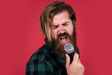 Kareli gömlek giyen sakallı bir adam. Rock müzik. Erkek karaoke şarkıcısı. Olgun karizmatik erkek vokalist. Mikrofonda şarkı söyleyen sakallı adam. Sahnede özgüven ve karizma