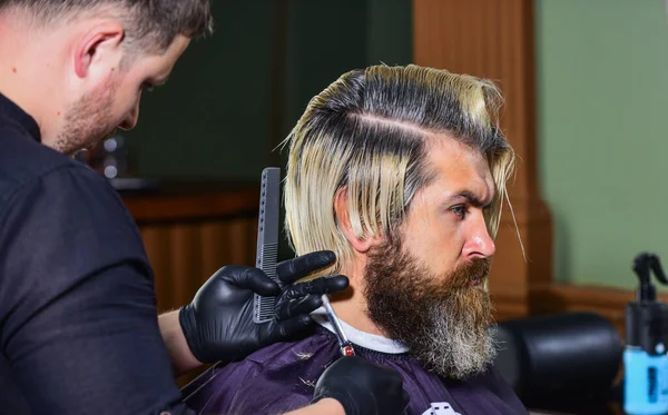 Barbeiro ou ferramenta de cabeleireiro. Um hipster brutal na barbearia. cliente barbudo visitando cabeleireiro. Hora do novo corte de cabelo. o homem olha para o reflexo do espelho. maduro bonito homem com cabelos longos — Fotografia de Stock