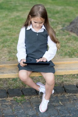 Okul üniformalı küçük bir çocuk dokunmatik ekran ya da dokunmatik ekran parmak basın tablet bilgisayar simgesi açık tribünde oturuyor, e-okul