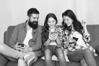 Oyun uygulaması oynat. İnternette aile sörfü. Aile eğlencesi. Çevrimiçi aile. Anne baba ve kızı kanepede dinleniyor. Aile hafta sonunu internette geçiriyor. Küçük kız anne babasıyla akıllı telefon kullanıyor.