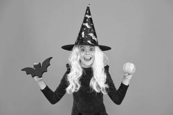 Ijesztően gonosz Halloween. A kis gonosz boszorkány gyerek denevért és tököt tart. Boldog lány gonosz boszorkány jelmezt visel. Kis gonosz boszorkány divatos és félelmetes megjelenéssel. — Stock Fotó