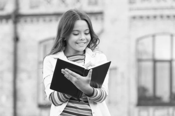 L'accès à bien plus qu'un simple livre. Concept de connaissance. Une petite fille tient le livre. Fille avec le fond de bâtiment d'école de livre. Livre de la bibliothèque. Prendre des notes. Poète inspiré. Talentueuse écolière mignonne — Photo