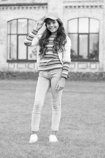 Kendi tarzında. çocukluk mutluluğu. Uzun kıvırcık saçlı mutlu kız. Güzel çocuk dışarıda gülümsüyor. Çocuk güzelliği ve moda. Neşeli liseli kızlar şapka takar. Gençlik gündelik tarzında. Kuaför konsepti