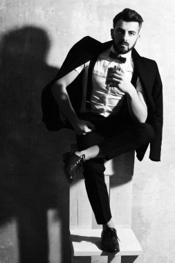 Sakallı adamın elinde matara, stüdyo duvarında ciddi bir yüz var.