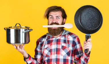 Aç adam. Kareli gömlekli profesyonel aşçı. Sakallı koca. Restoranda. İsimsiz dökme demir pişirme kabı. Yapışkan olmayan kaplamalı politetrafluoretilen teflon. Sağlıklı yemek pişirmek.